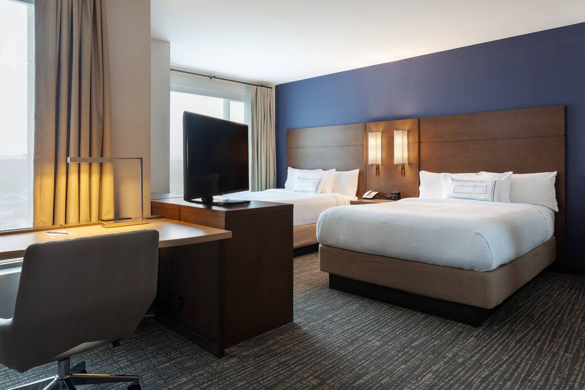 Habitación de hotel con cama, escritorio, silla, televisor y dos lámparas de noche.