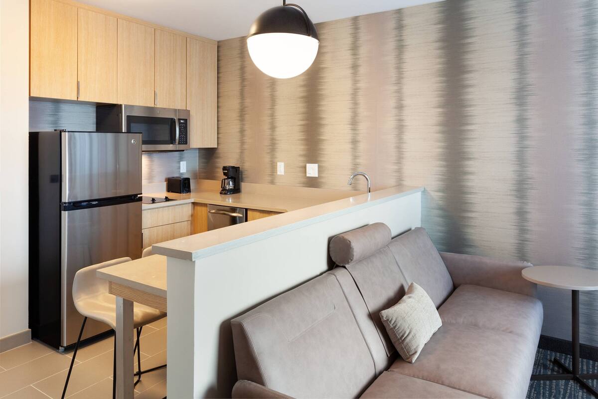 Una cocina moderna con electrodomésticos de acero inoxidable, una isla central y una zona de estar con sofá y una mesita.