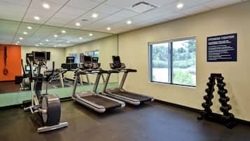 Un gimnasio con cintas de correr, elípticas y un soporte para mancuernas.