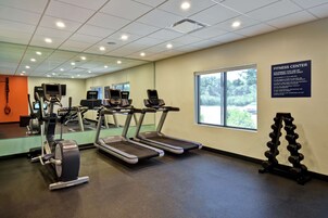 Un gimnasio con cintas de correr, elípticas y un soporte para mancuernas.