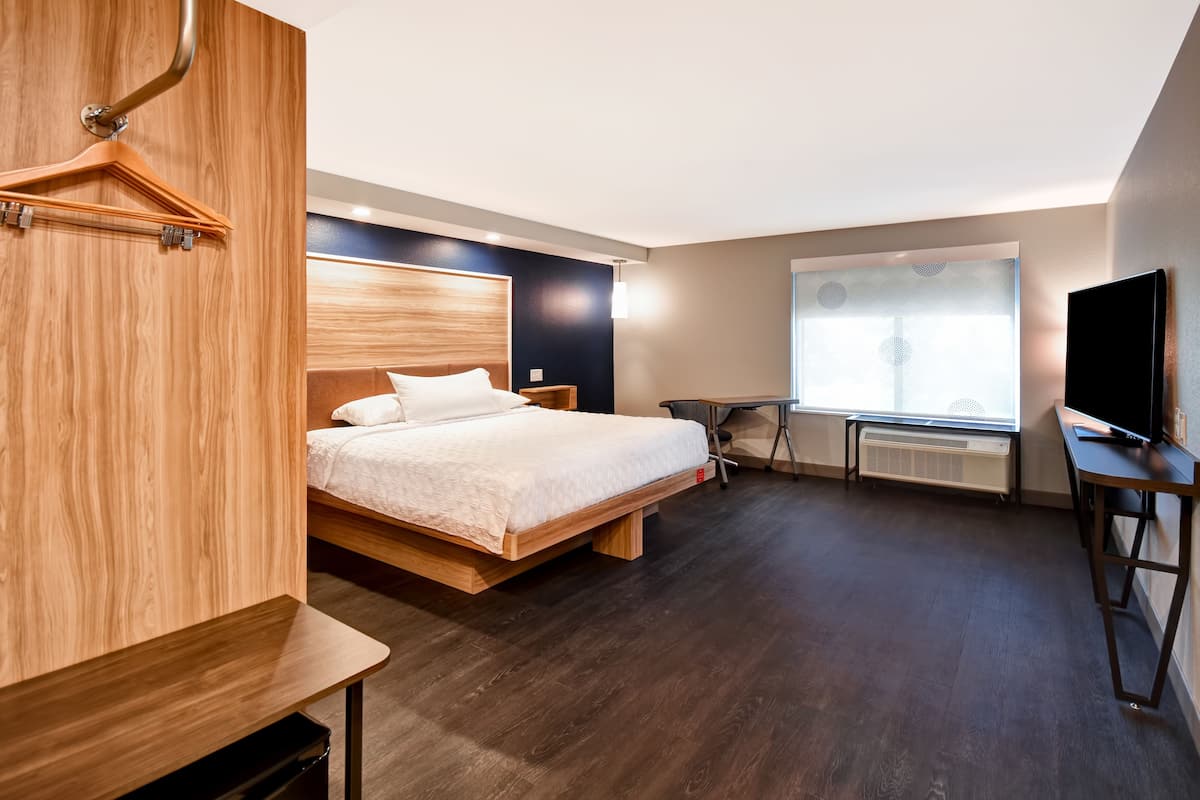 A modern hotel room with a wooden bed, a desk, a television, and a window with a view.
