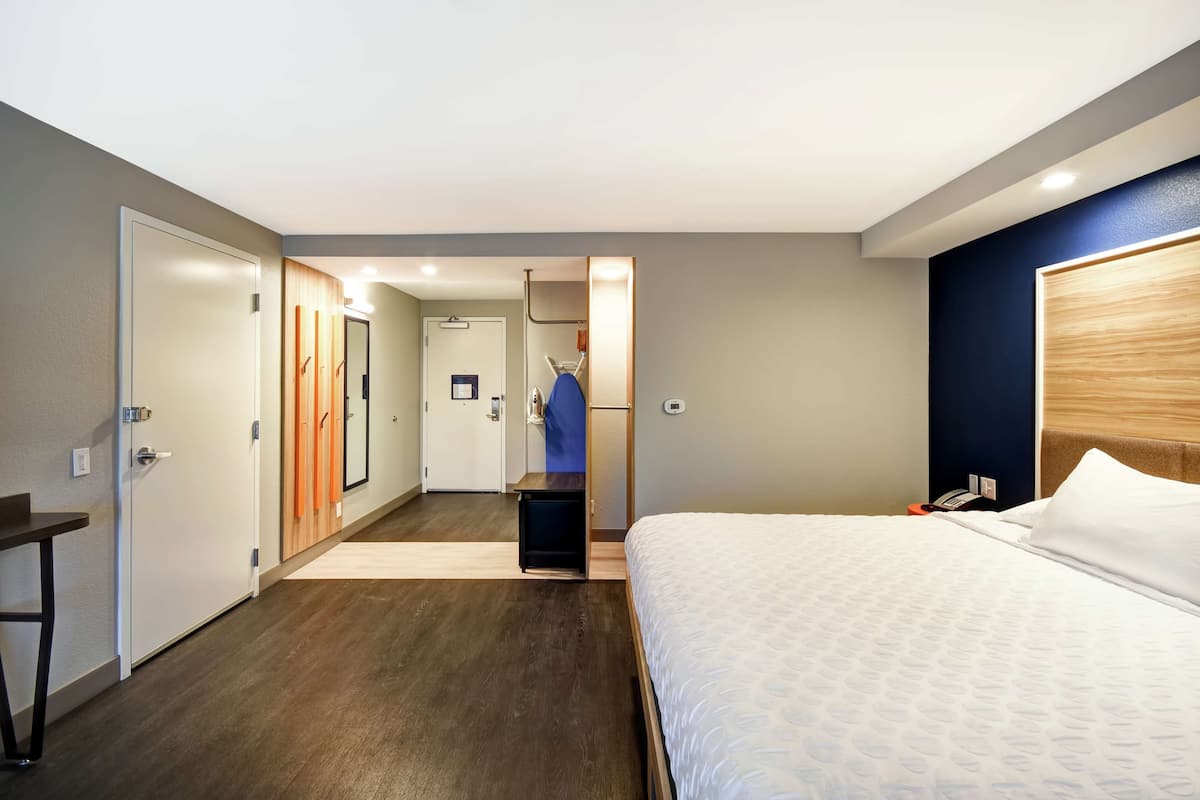 A hotel room with a large bed, a desk, and a mirror. There is a door leading to a bathroom and a hallway.