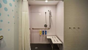 Een badkamer met een douche, handgrepen en een bankje.