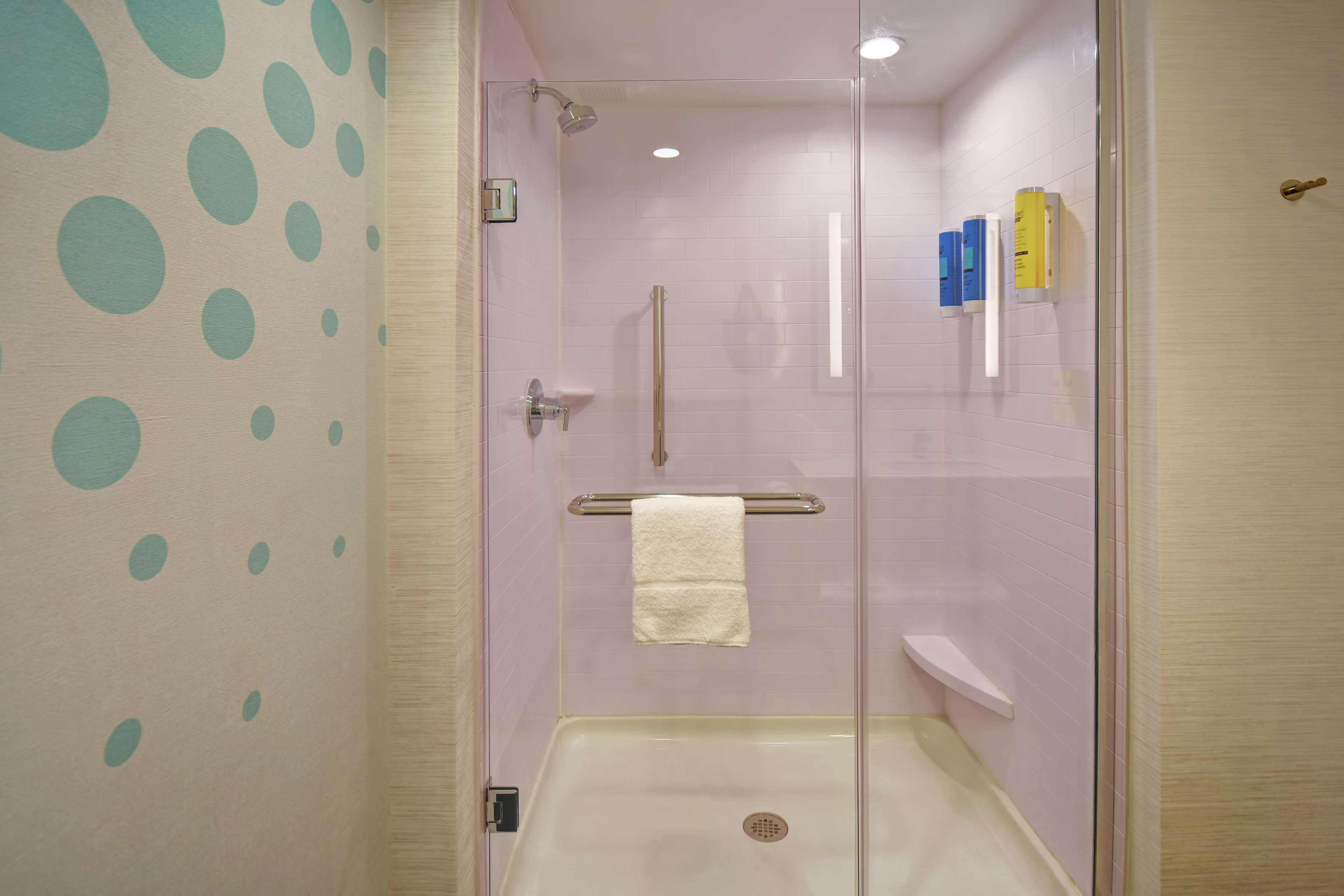 A glass-enclosed shower stall with a white sink, a towel rack, and a handrail.
