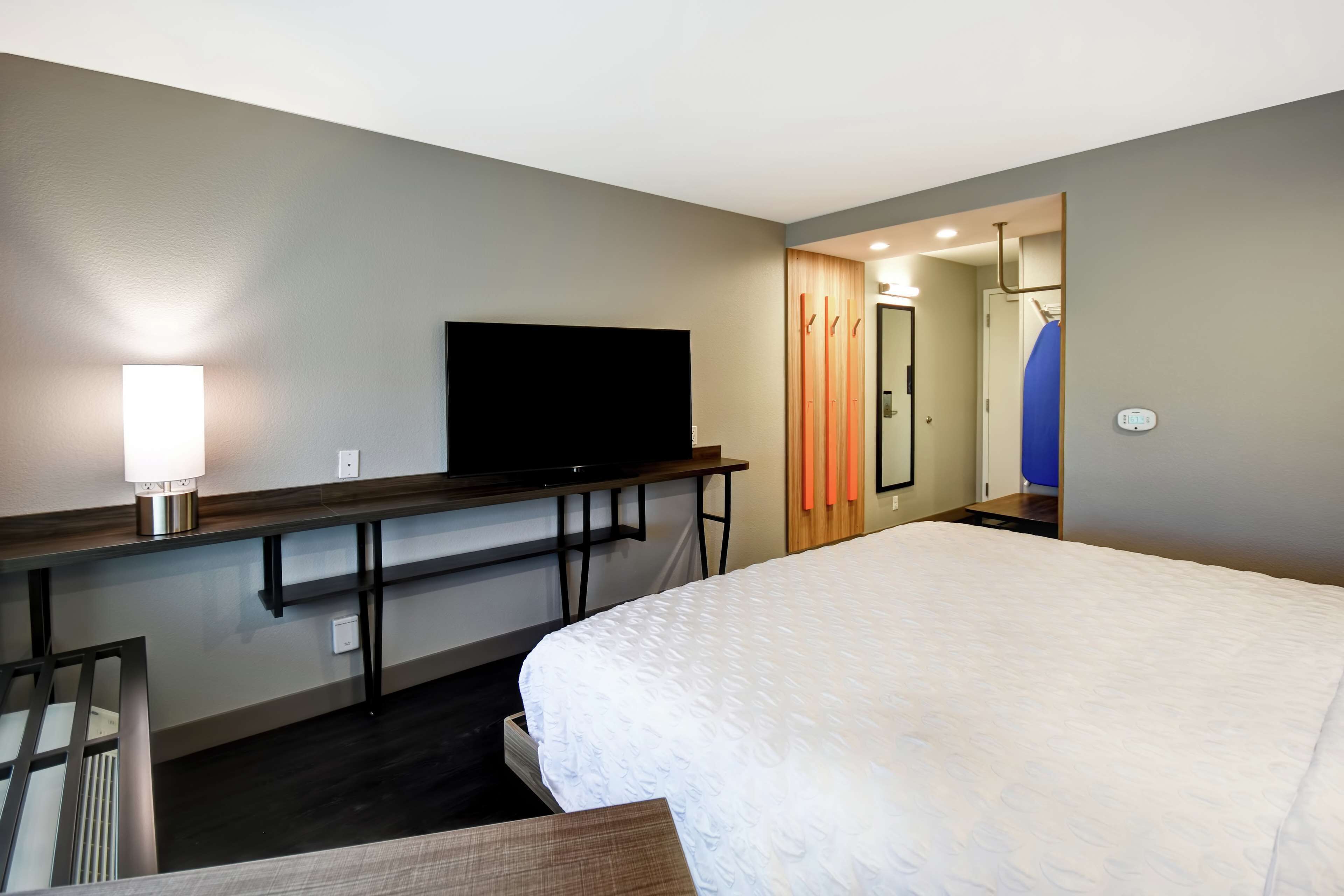 A hotel room with a bed, a flat-screen TV, a desk with a lamp, and a mirror.