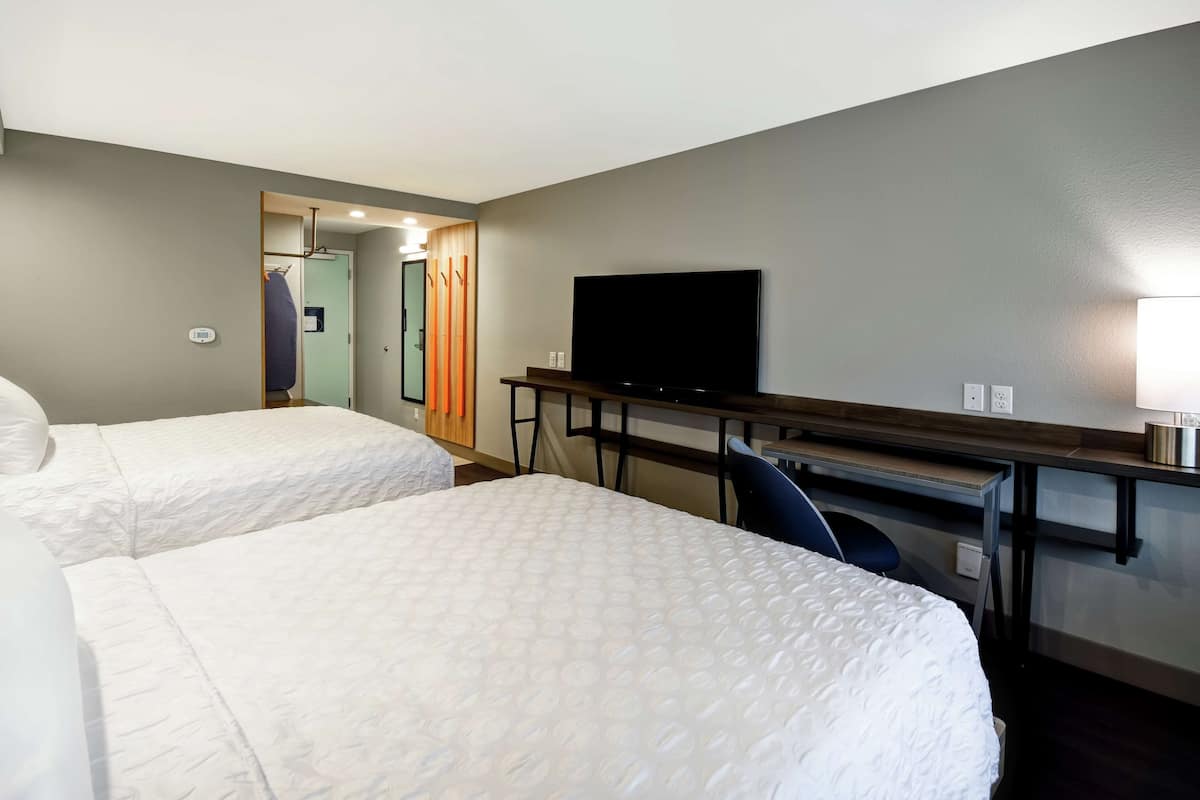 A hotel room with two beds, a desk, a chair, a television, and a mirror.