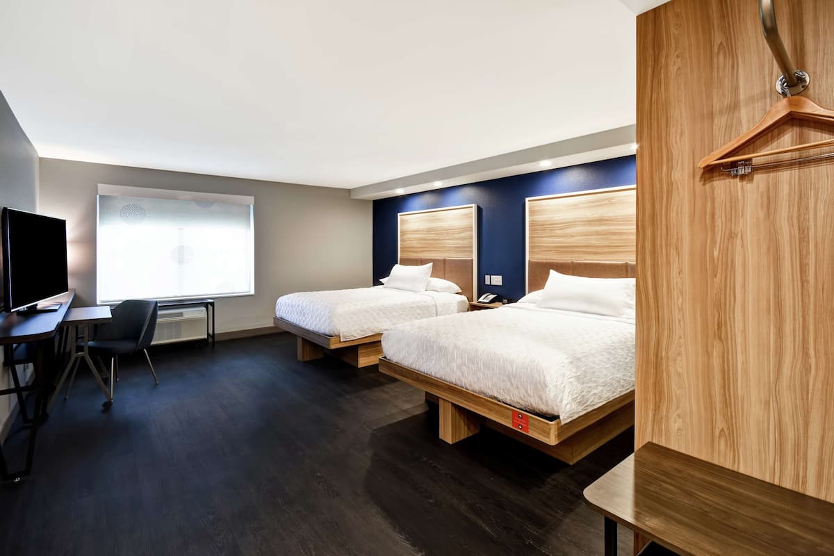 A hotel room with two beds, a desk, and a TV.