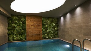 Une piscine intérieure moderne, dotée d’un sol carrelé de bleu, entourée de murs agrémentés d’un jardin vertical et de panneaux en bois.