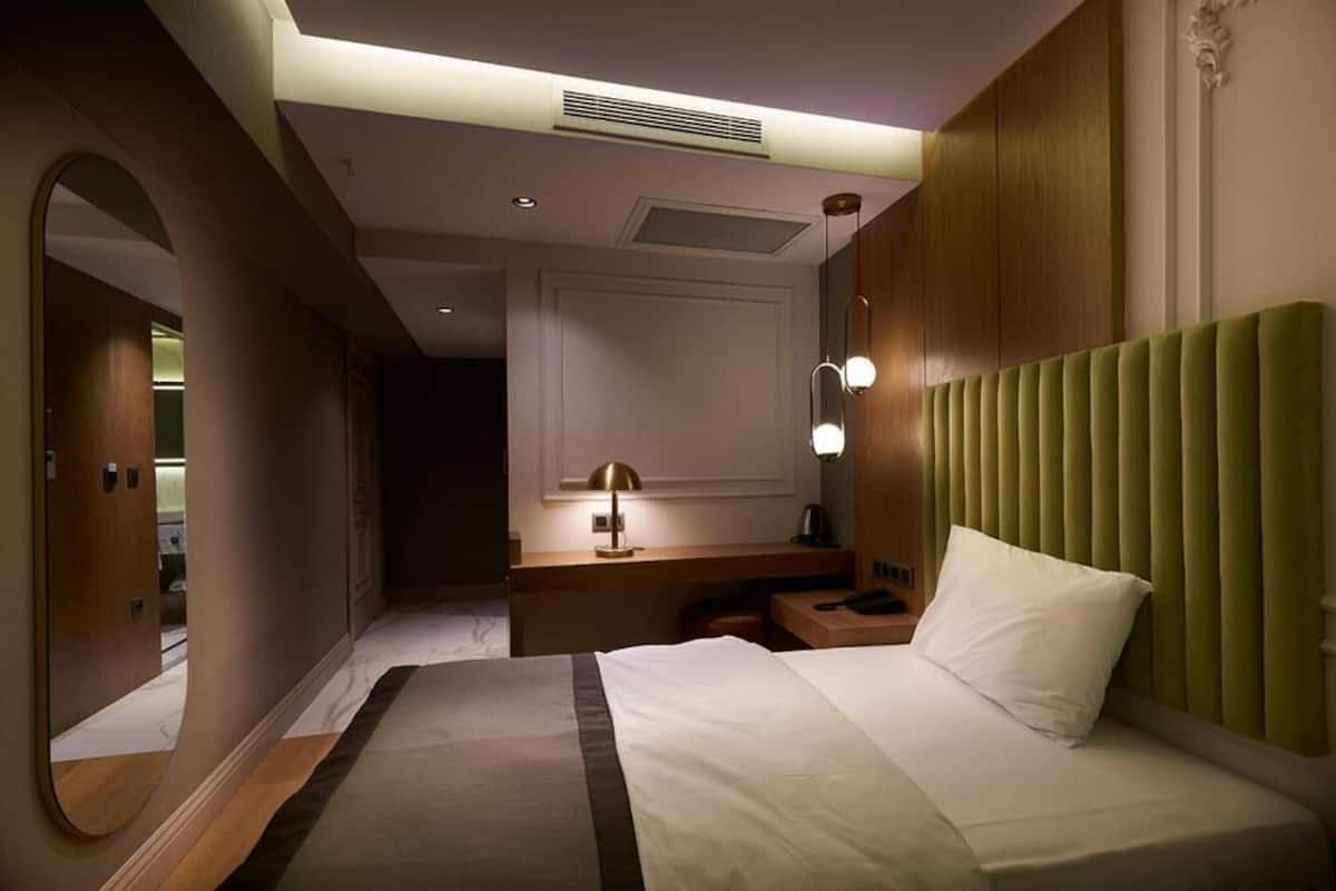 A hotel room with a bed, bedside table, lamp, and a mirror.