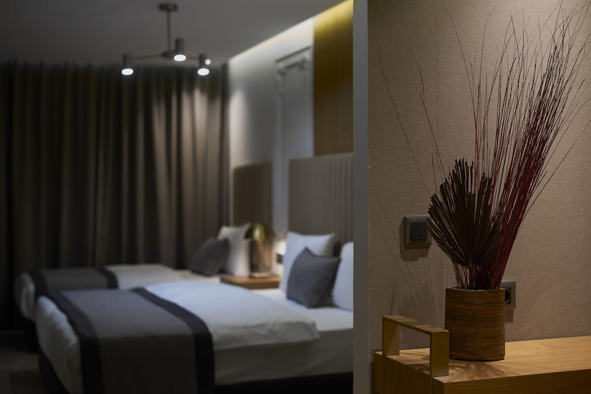 A modern hotel room with a large bed, bedside tables, and a decorative vase on a wooden nightstand.
