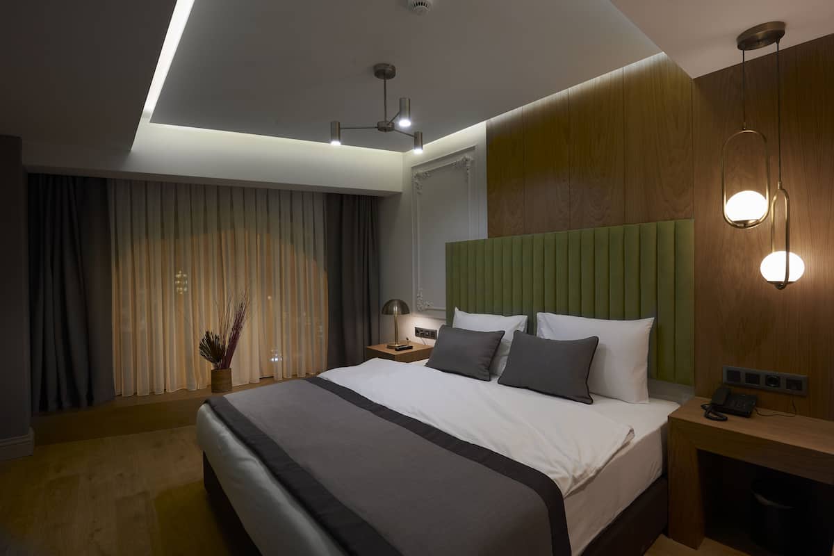 A modern hotel room with a large bed, a wooden headboard, a bedside table with a lamp, and a nightstand with a phone.