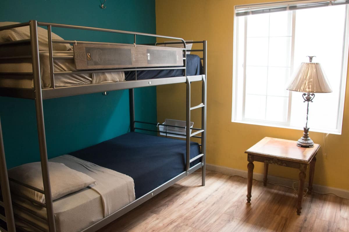 A bunk bed room with a small table and lamp by a window.