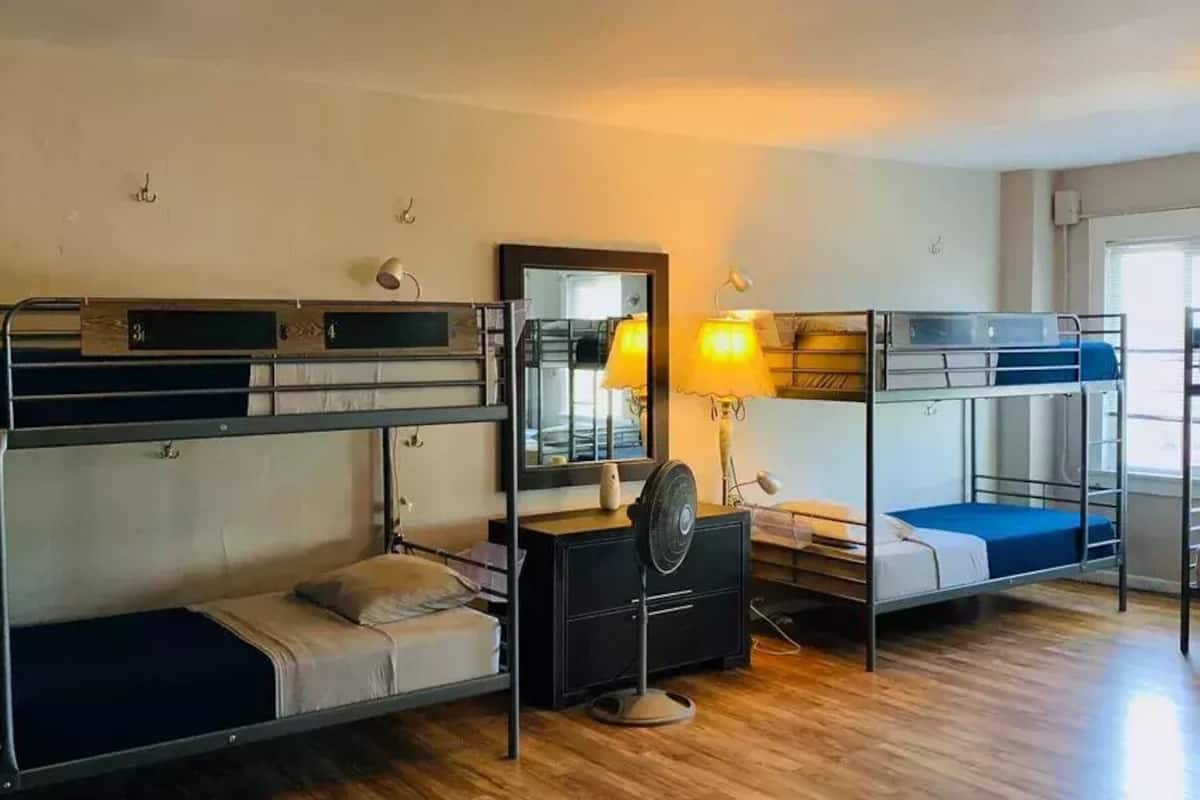 A dormitory room with bunk beds, a dresser, a mirror, and a lamp.