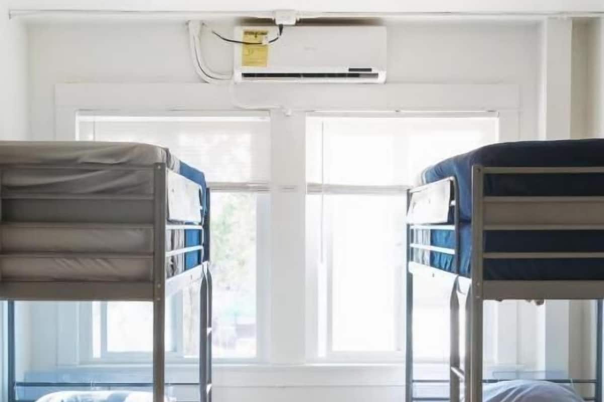 A room with two bunk beds, wooden flooring, a window with blinds, and an air conditioning unit.