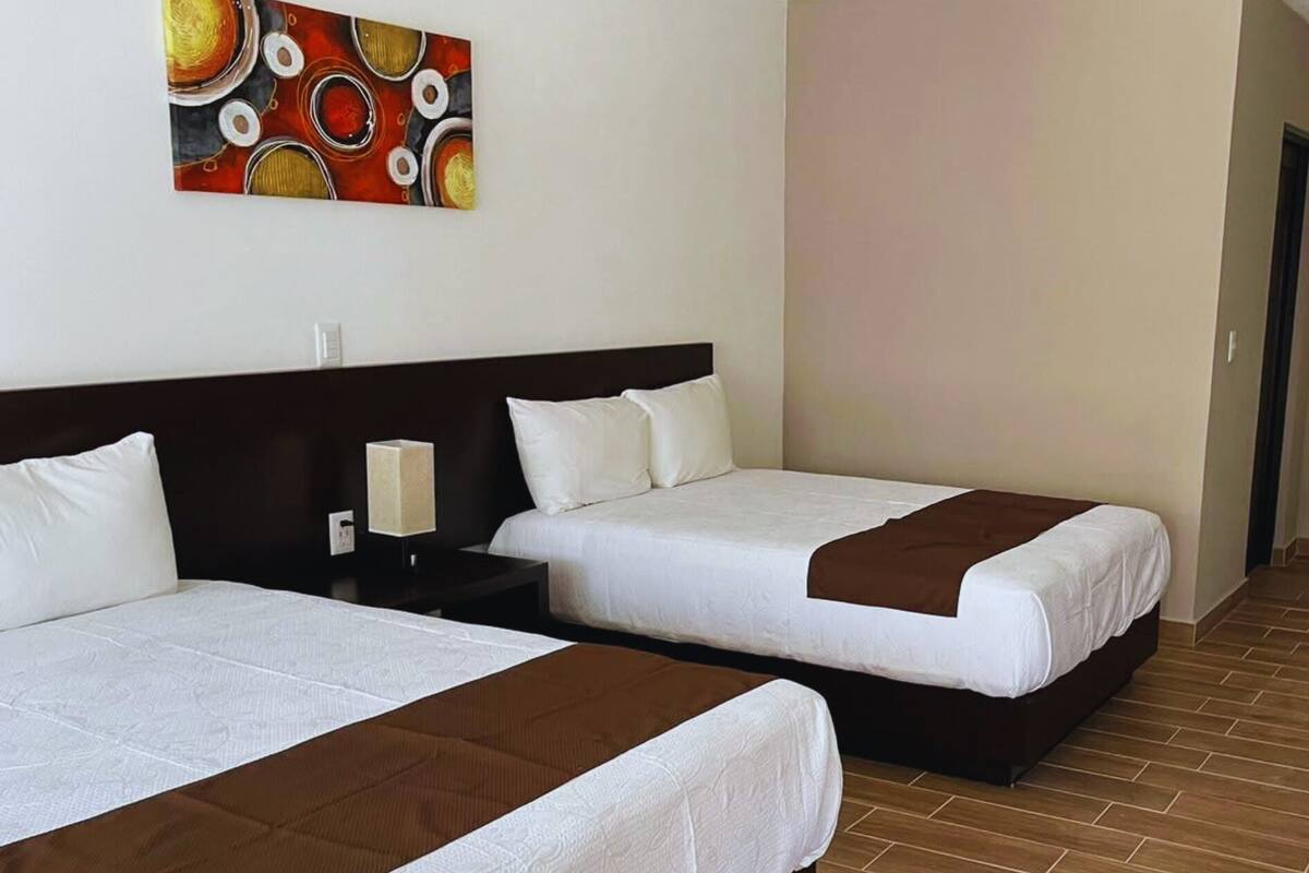 Une chambre d’hôtel avec deux lits, une table de chevet, une lampe et un tableau au mur.