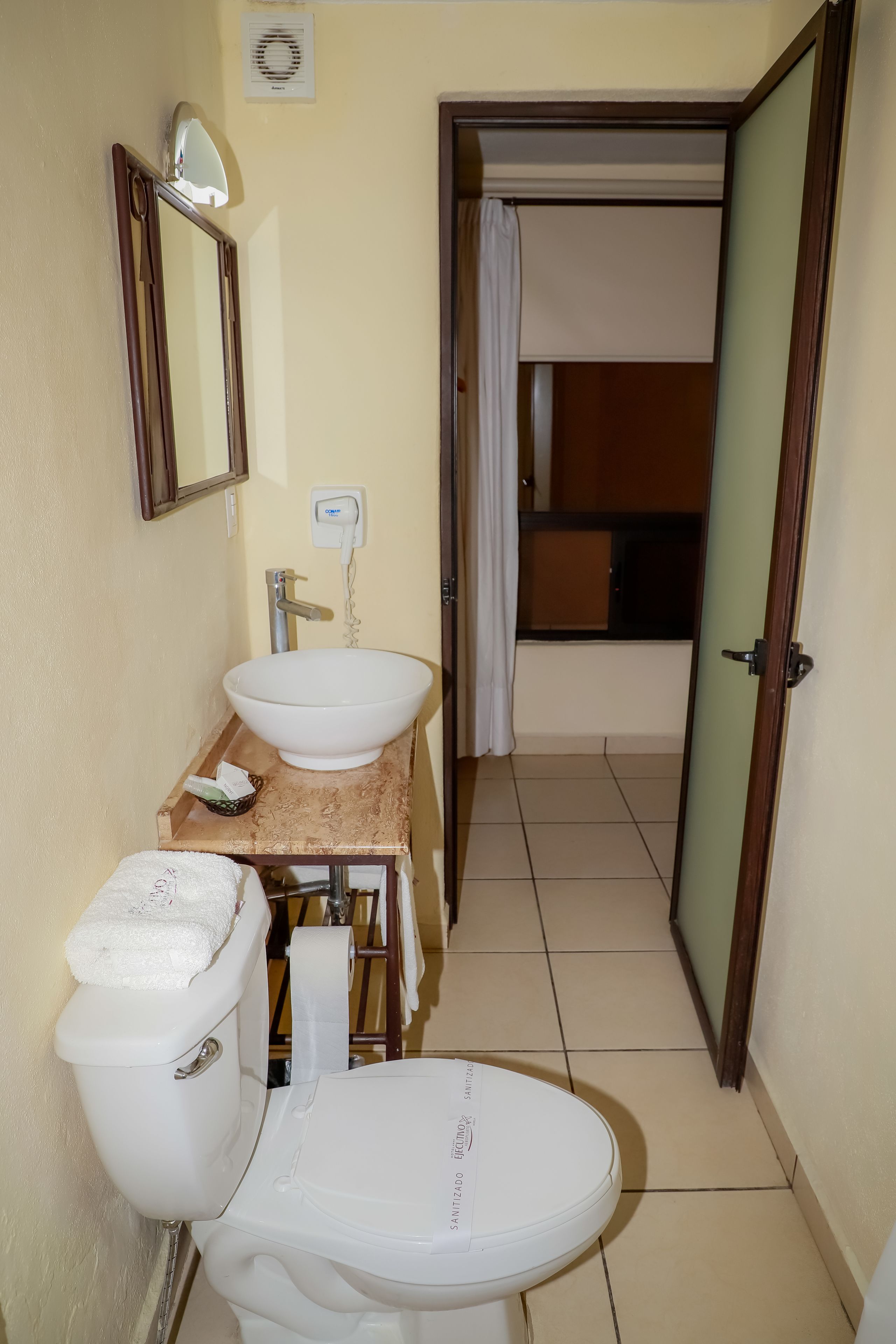 Un baño con inodoro blanco, lavamanos y espejo.