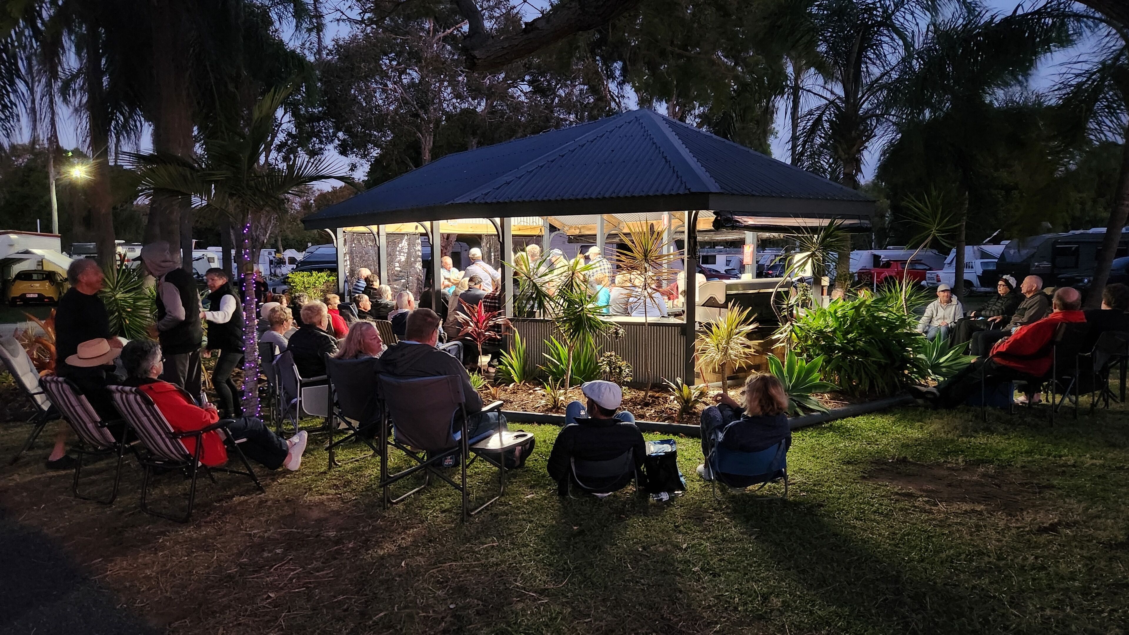 A gazebo with a glass enclosure surrounded by chairs and people.