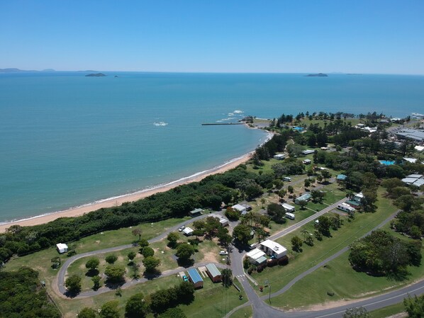 Vue aérienne d’une zone côtière comprenant une plage, des espaces verts et des immeubles résidentiels.