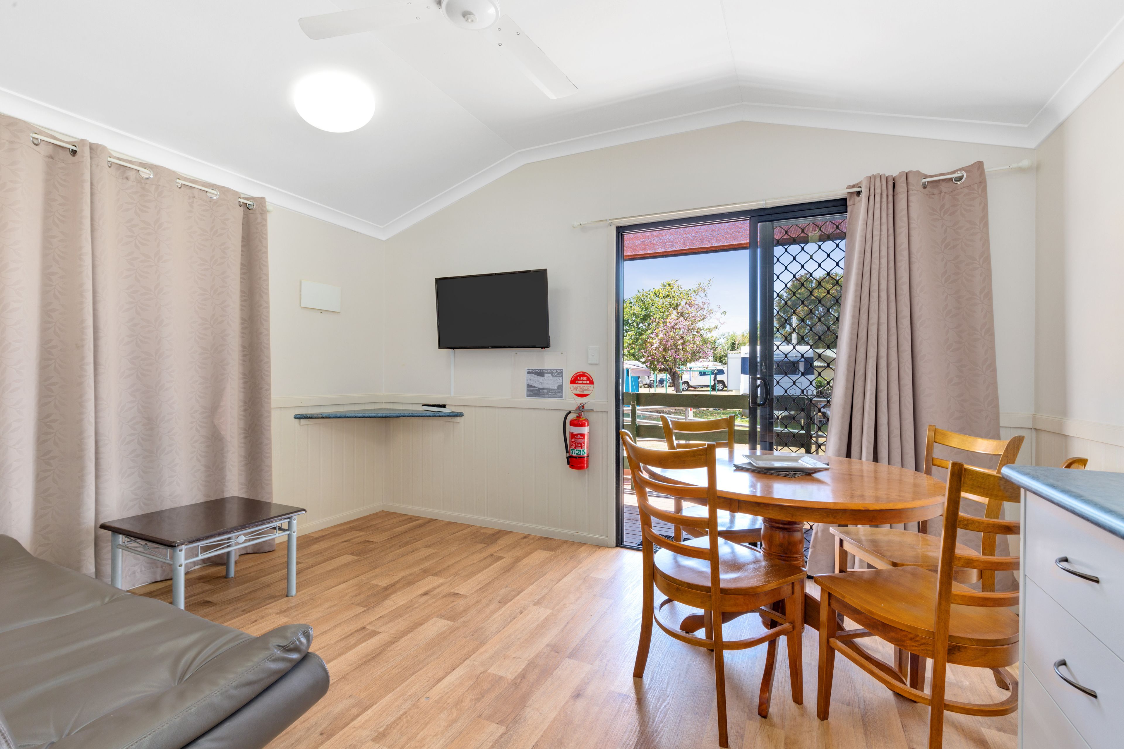 A room with a wooden dining table, chairs, a sofa, a television, and a fire extinguisher.