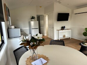 Une cuisine moderne avec des appareils électroménagers blancs, un coin repas avec une table et des chaises blanches, et un téléviseur à écran plat fixé au mur.