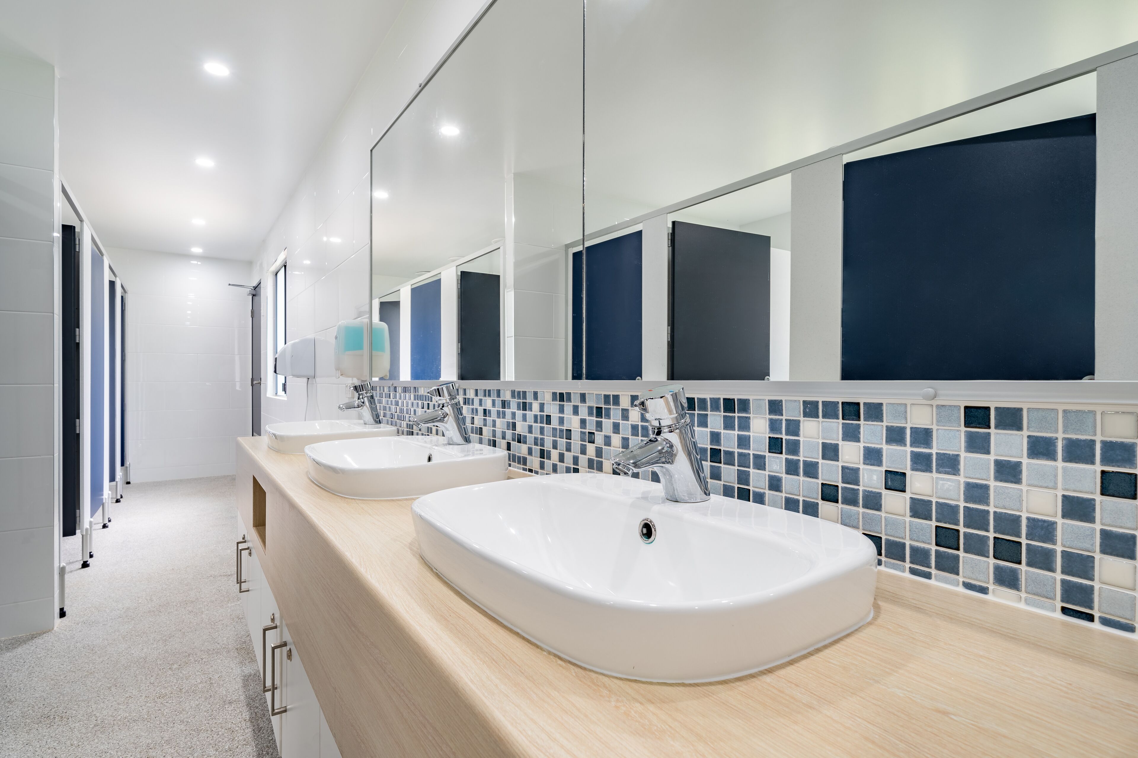 A modern bathroom with three sinks, a mirror, and a tiled backsplash.