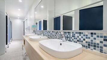 A modern bathroom with three sinks, a mirror, and a tiled backsplash.