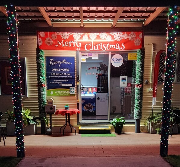 Zona de recepción con temática navideña, con un cartel que dice 'Merry Christmas', un mostrador de recepción y un cartel que indica 'G'DAY PARKS'.