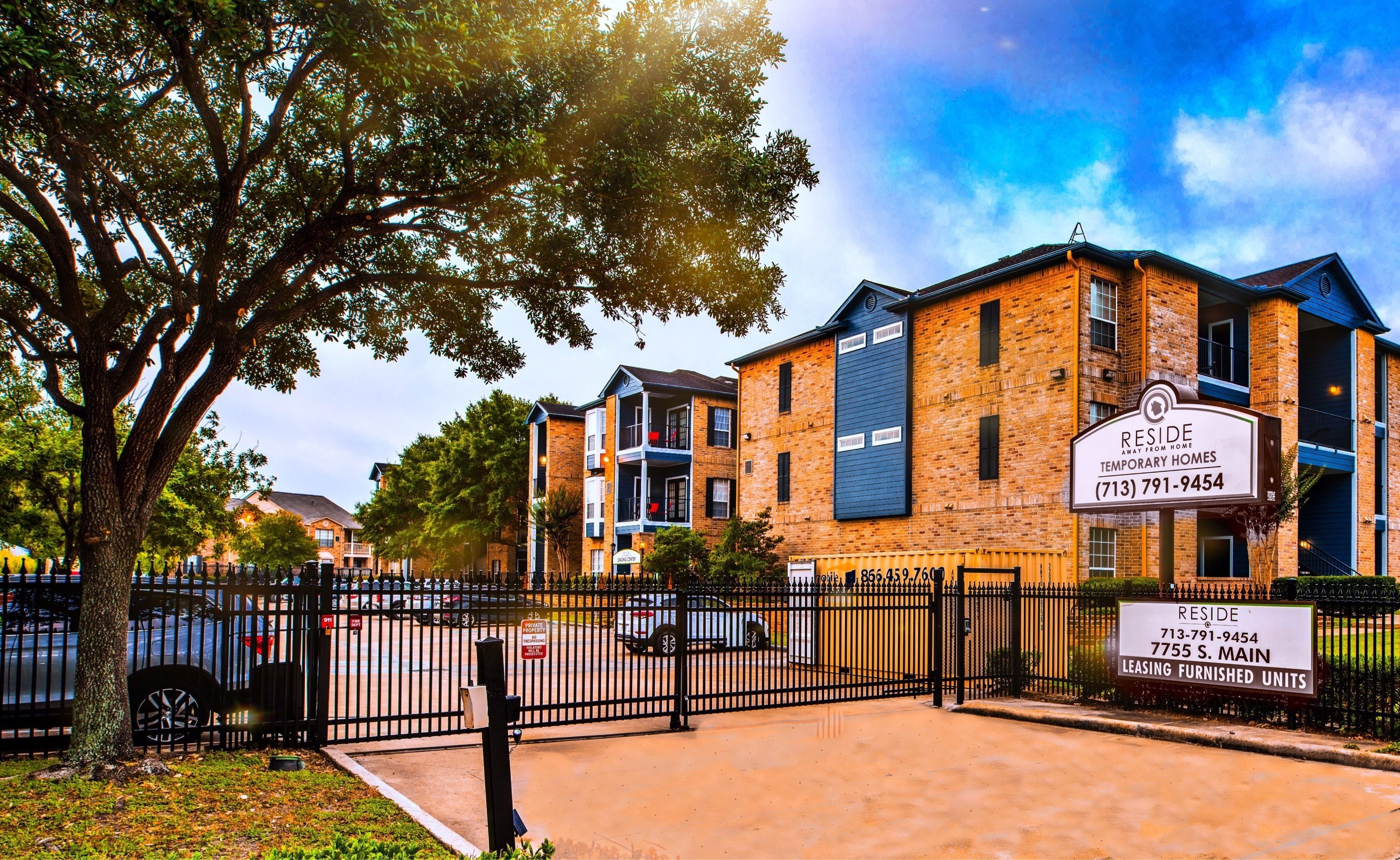 A brick building with multiple floors, a sign for 'RESIDE Temporary Homes', and a fenced parking area.
