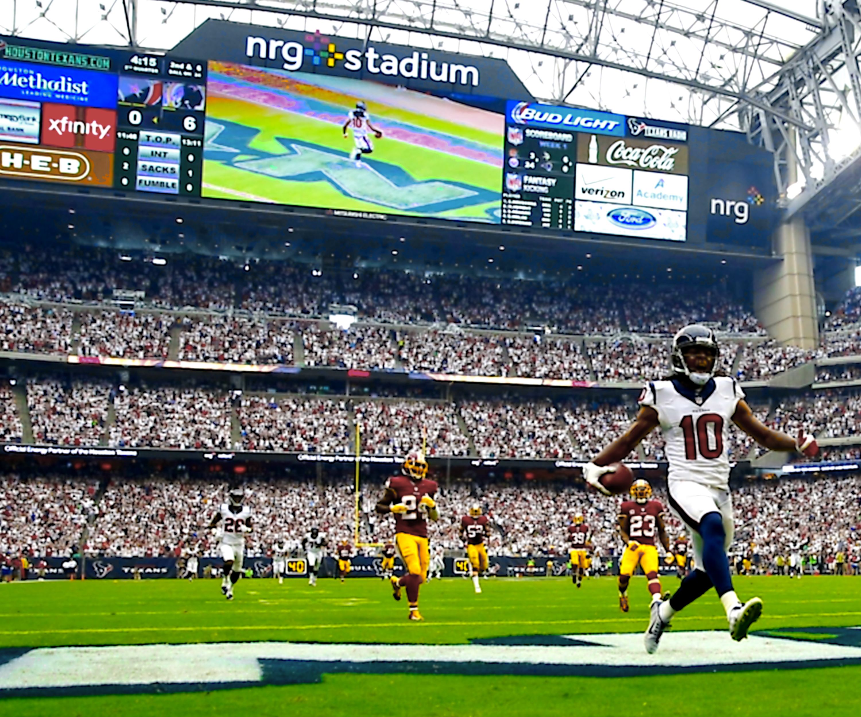 A football stadium with multiple levels of seating, a large scoreboard, and advertisements.