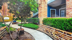 A courtyard with a brick building, a tree, and a sign for a leasing center. - The Reside (Houston)
