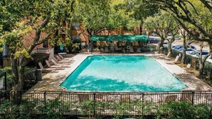 A rectangular swimming pool surrounded by a fence, with lounge chairs and a covered seating area in the background. - The Reside (Houston)