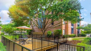 A wooden deck with outdoor furniture, a tree, and a brick building in the background. - The Reside (Houston)