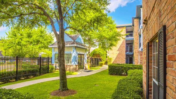 A well-maintained courtyard with a tree-lined pathway leading to a building with a blue facade. - The Reside (Houston)