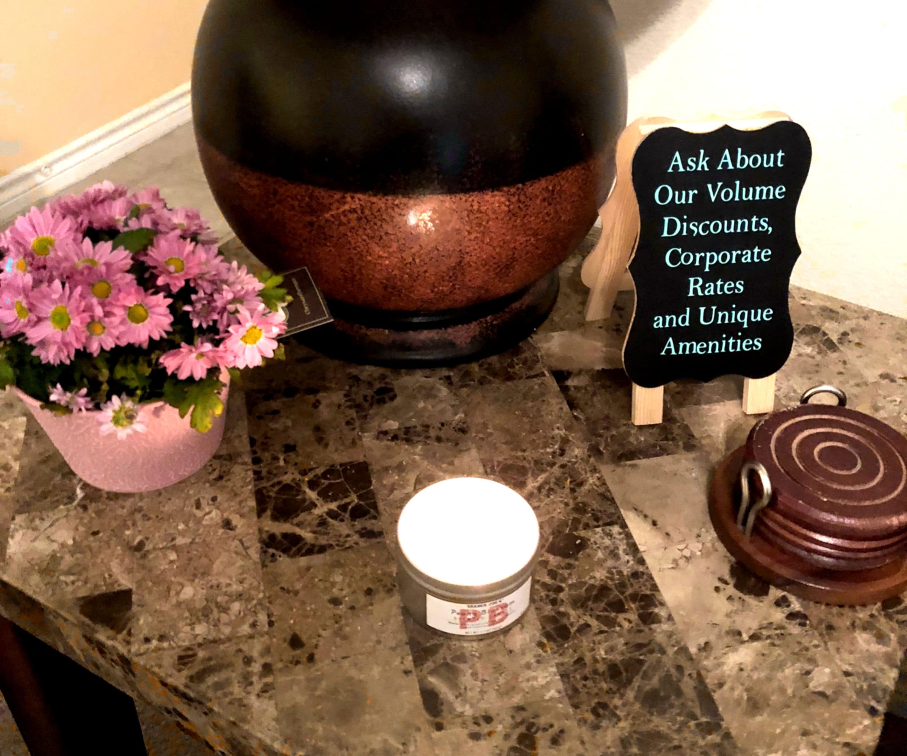 Una encimera de mármol con una olla grande negra y de cobre, una pequeña maceta con flores rosas, una vela y un letrero que ofrece descuentos por volumen y servicios.