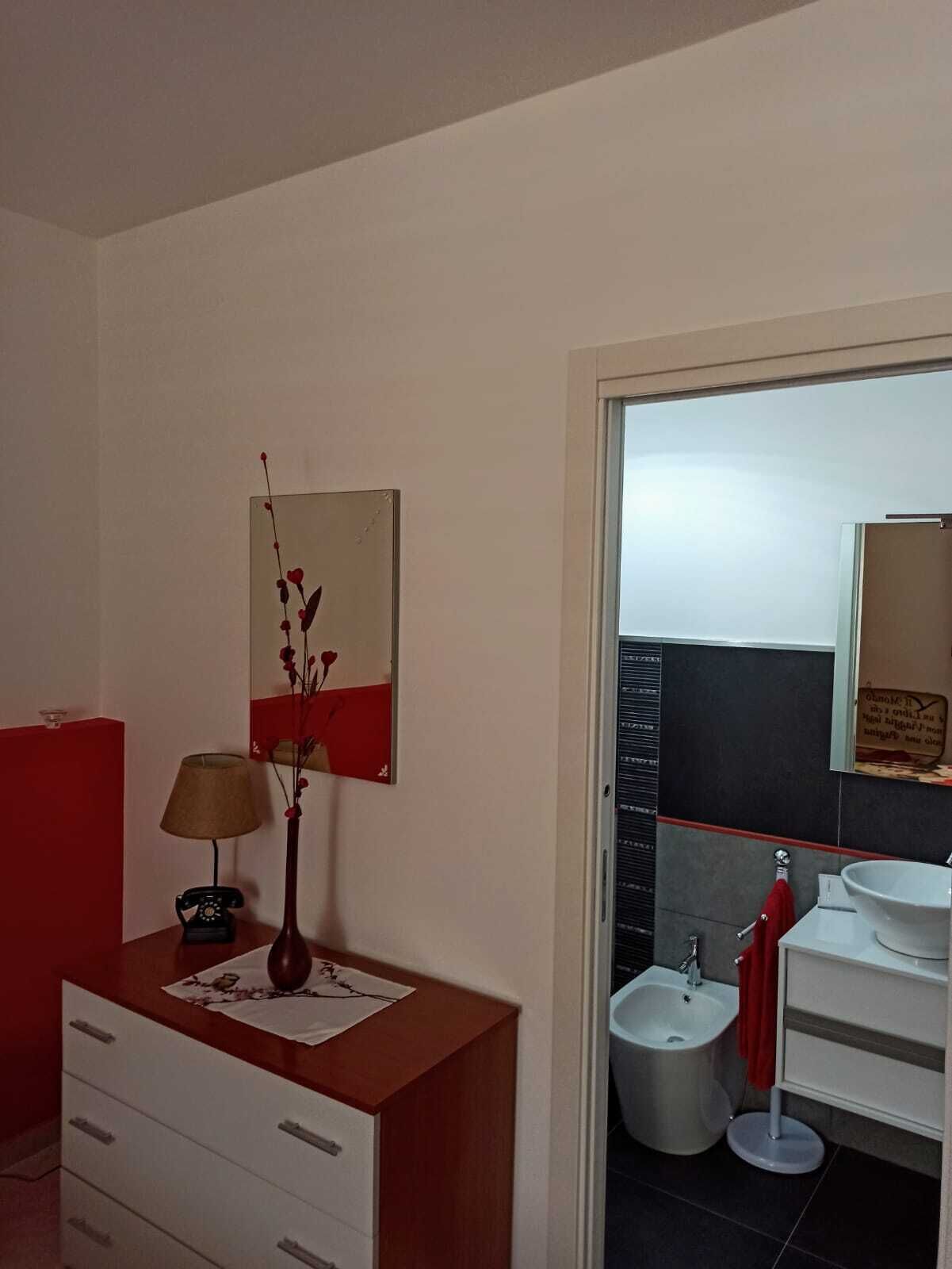 A bathroom with a red vanity, a mirror, a vase with red flowers, and a bidet.