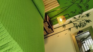 Quarto com parede verde, cama de madeira, espelho e luminária pendente.