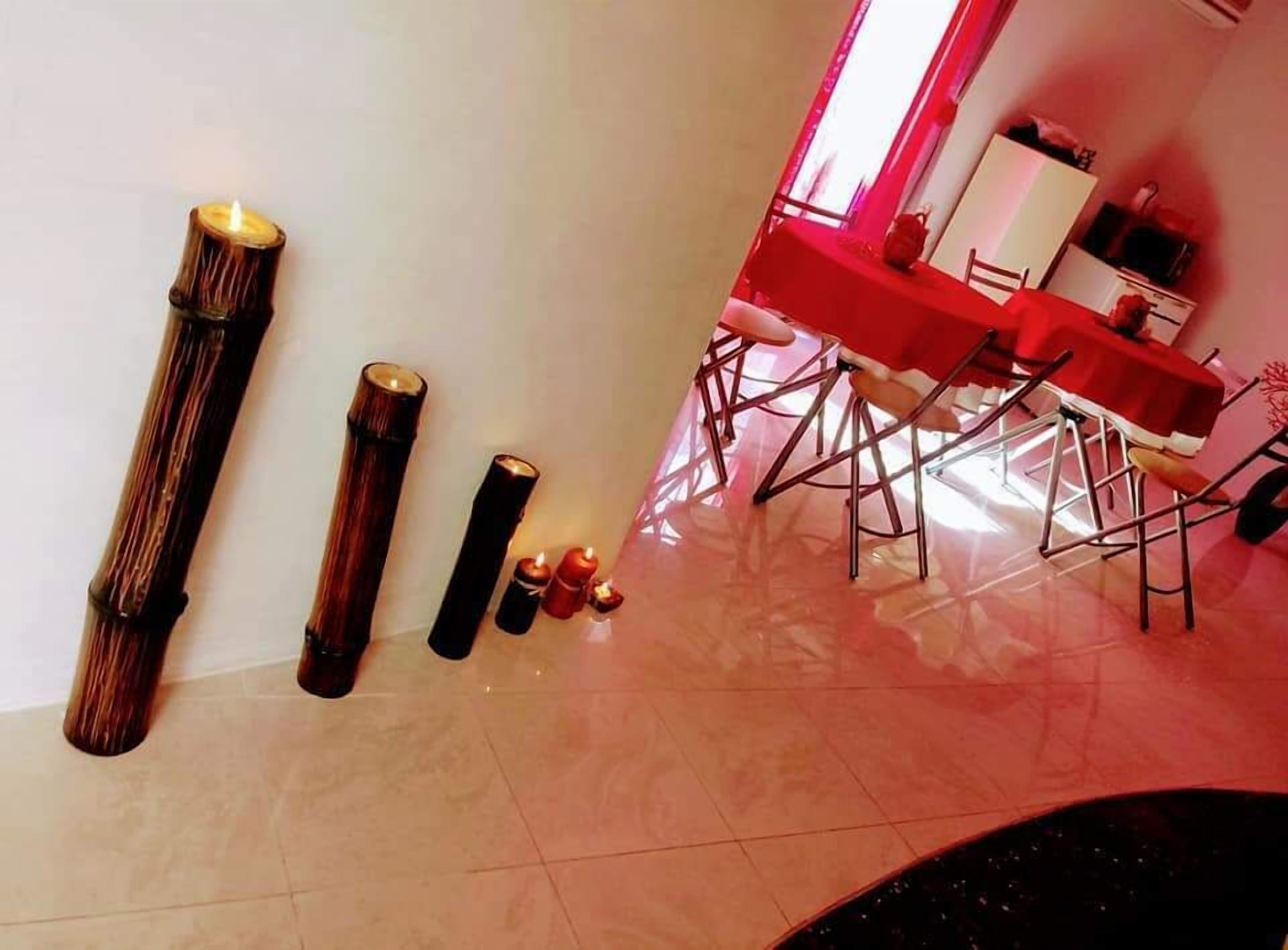 A dining area with a red table and chairs, a tall candle, and a small table with candles.