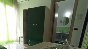 Quarto com mesa de madeira, armário verde e área de cozinha visível por uma porta aberta.