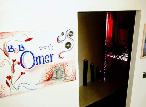 A hallway with a sign reading "B&B Omer" and a view into a room with a red curtain and a chair. - Omer B&B (Sciacca)