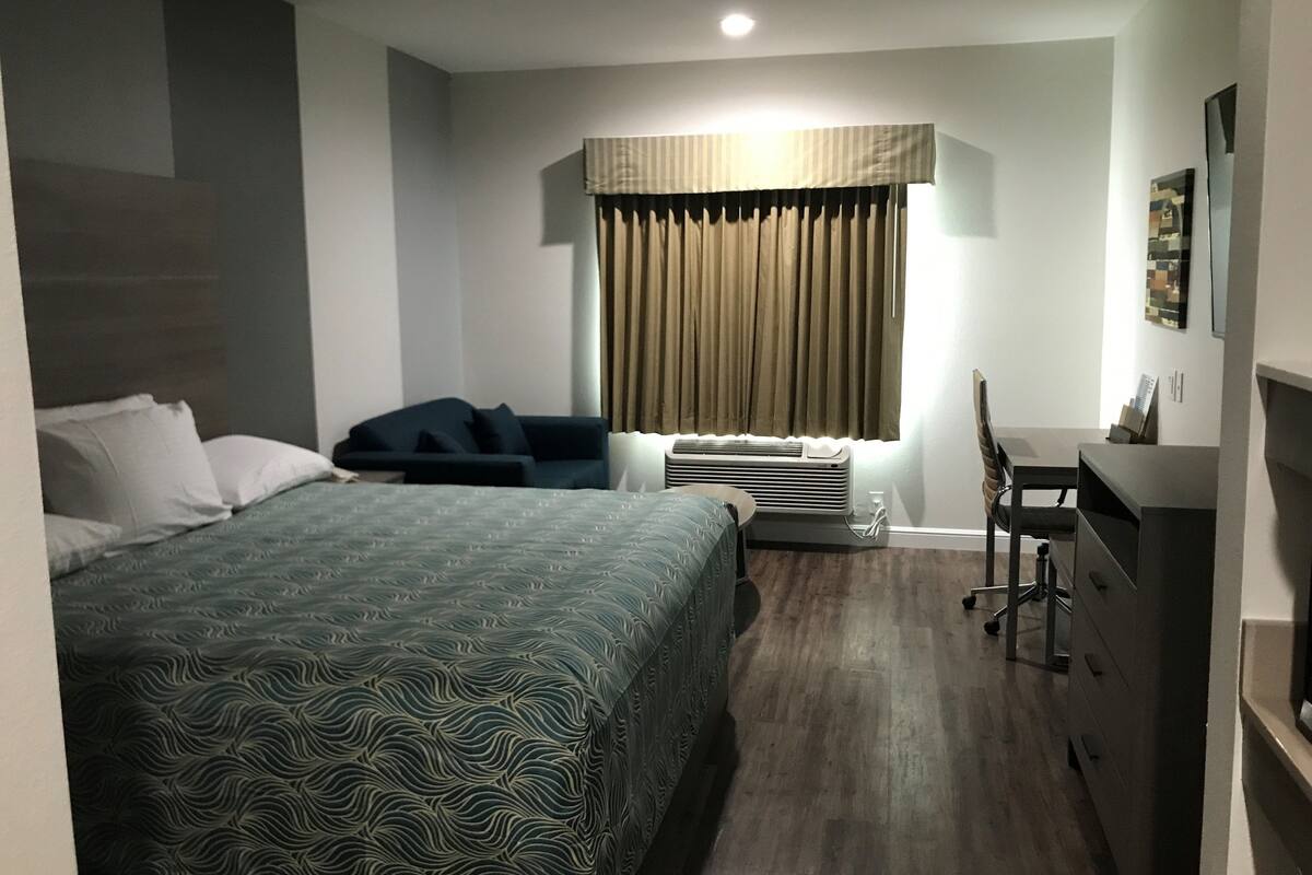 Una habitación de hotel con cama, escritorio, silla, cómoda y ventana con cortinas.