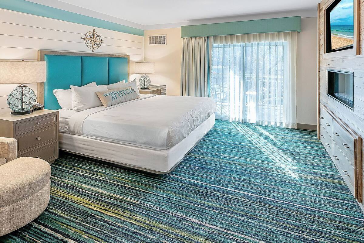 Une chambre d’hôtel avec un grand lit, une table de chevet, une chaise et une vue sur la plage par la fenêtre.