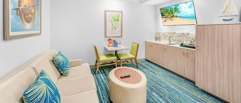 Habitación con sofá, sillas, una mesita, televisión y un área de cocina.