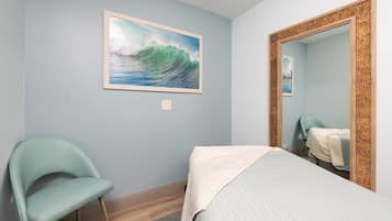 Un dormitorio con cama, una silla, un cuadro de una ola y un espejo con marco tejido.