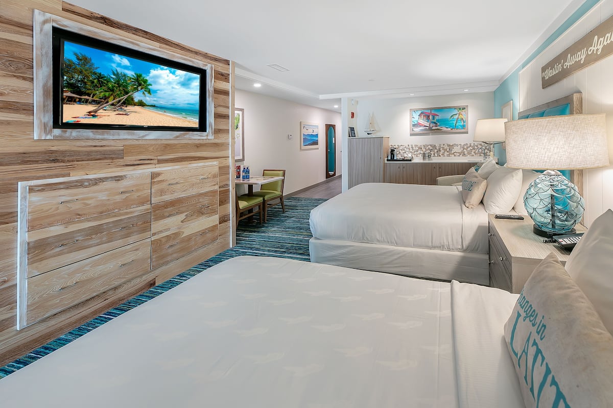 Une chambre d’hôtel avec un téléviseur fixé au mur, un lit, un bureau avec une lampe et une vue sur la plage.