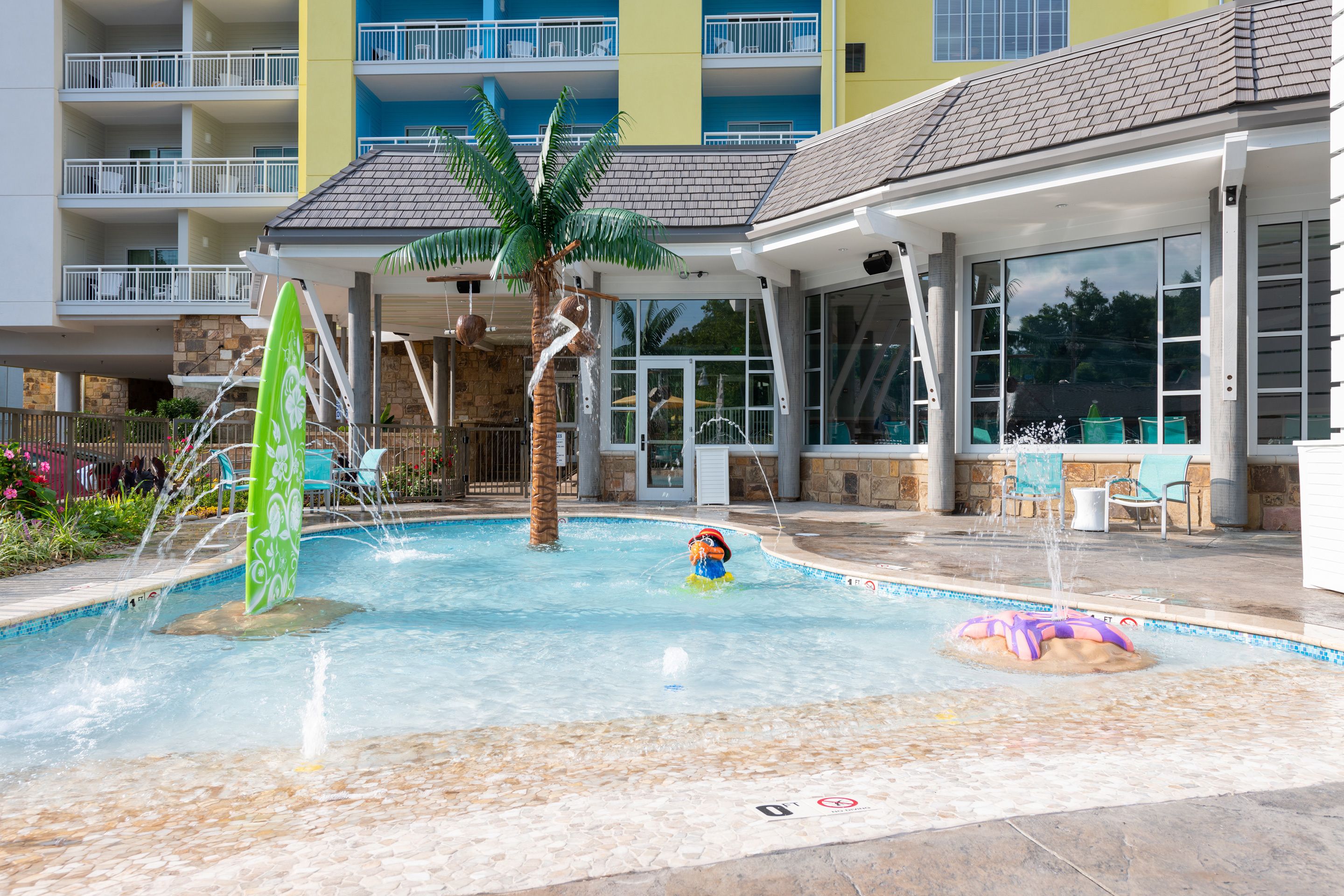 A swimming pool with a palm tree, a water slide, and lounge chairs.
