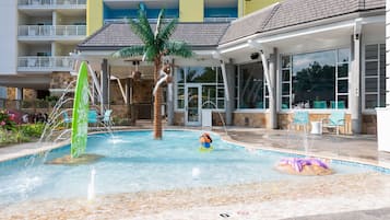 A swimming pool with a palm tree, a water slide, and lounge chairs.