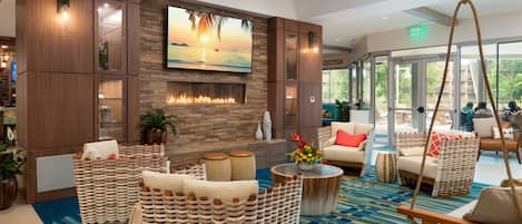 A spacious lobby with a large flat-screen TV, a fireplace, wicker furniture, and a patterned carpet.