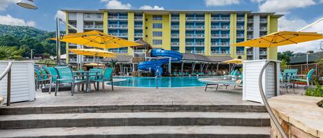 A hotel pool area with a blue water slide, outdoor seating, and a view of the hotel building.