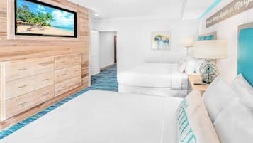 A hotel room with a large TV displaying a beach scene, a wooden dresser, a bed with white bedding, a blue carpet, and a painting of a parrot.