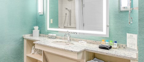 Un baño con un espejo grande, un lavamanos con encimera de mármol y una zona de ducha.